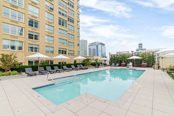 A large swimming pool surrounded by lounge chairs and umbrellas in front of a tall building.
